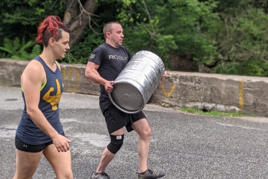 female coach supporting male athlete during a keg carry outside