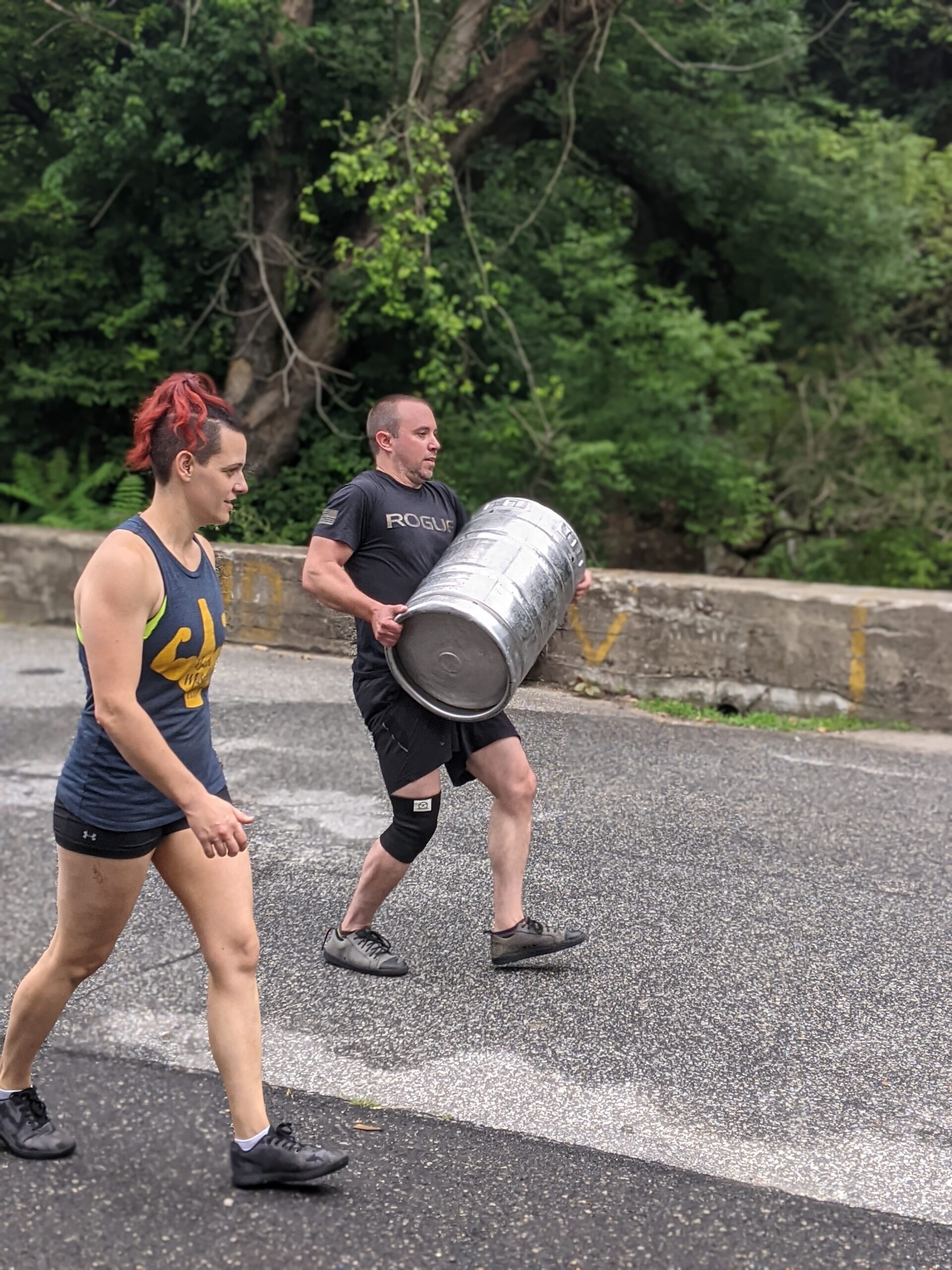 female coach supporting male athlete during a keg carry outside